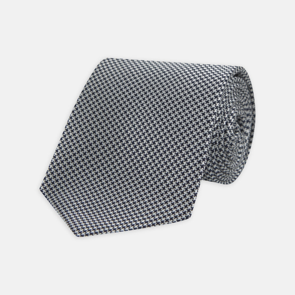 The Turnbull & Asser Navy Houndstooth Silk Tie features a refined small houndstooth pattern in navy, elegantly rolled and showcased on a white background.