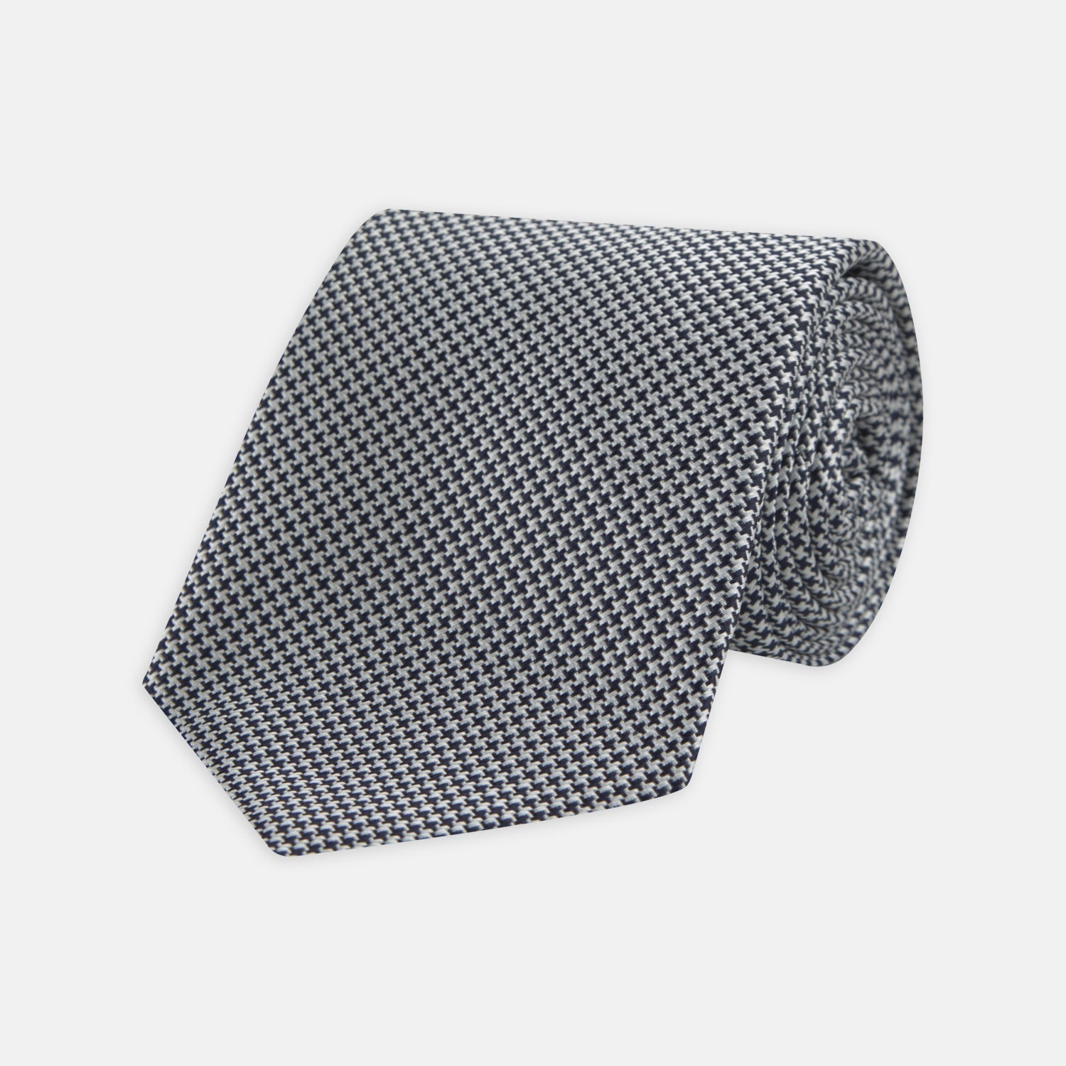 View 1 of product The Turnbull & Asser Navy Houndstooth Silk Tie features a refined small houndstooth pattern in navy, elegantly rolled and showcased on a white background.