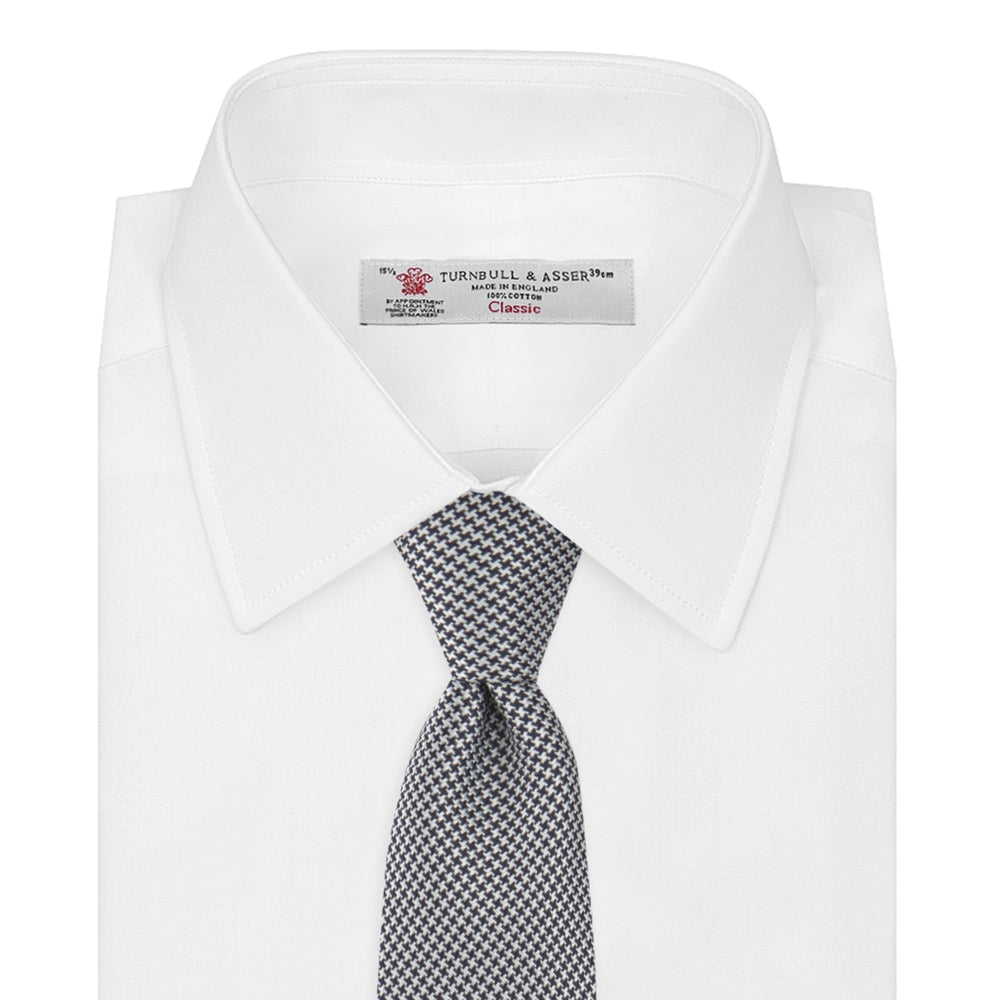 The Turnbull & Asser Navy Houndstooth Silk Tie features a refined small houndstooth pattern in navy, elegantly rolled and showcased on a white background.