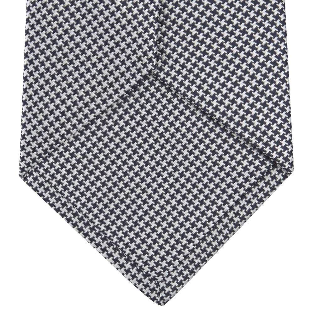 The Turnbull & Asser Navy Houndstooth Silk Tie features a refined small houndstooth pattern in navy, elegantly rolled and showcased on a white background.