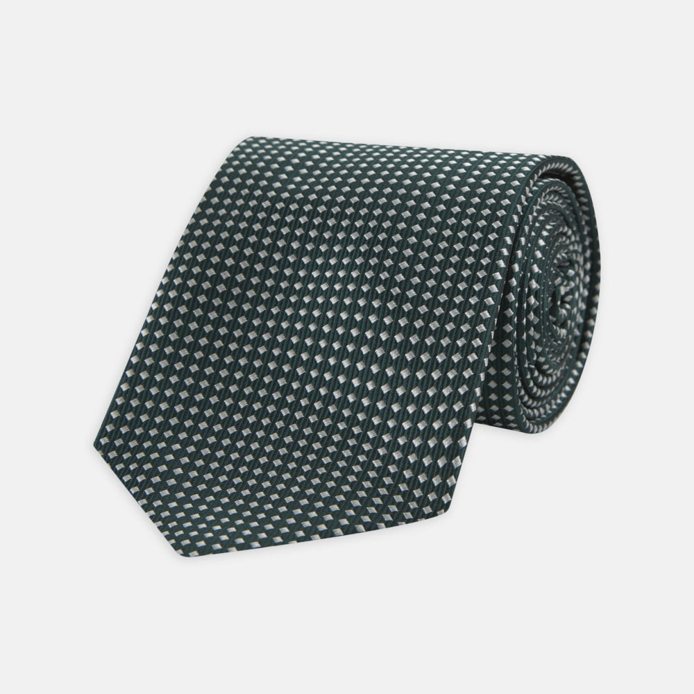 The Turnbull & Asser Forest Green and White Diamond Silk Tie features a geometric pattern of small, evenly spaced white diamonds on a forest green background, displayed rolled up on a white surface.