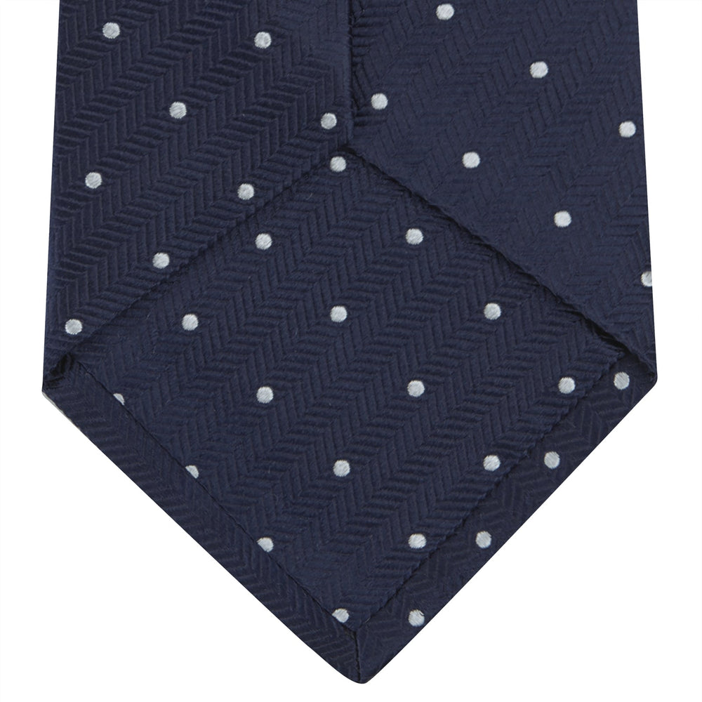The Navy and White Small Spot Herringbone Silk Tie from Turnbull & Asser features a classic navy herringbone pattern with small white polka dots, offering an elegant look suitable for any occasion.