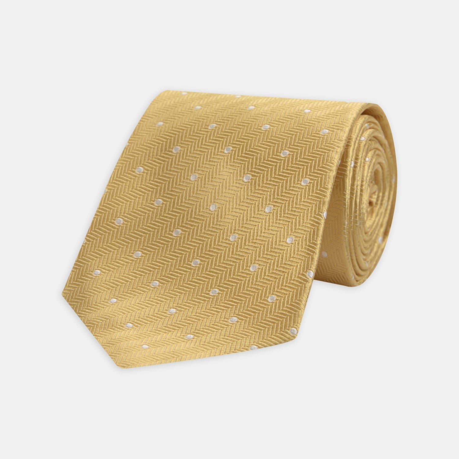 View 1 of product The Turnbull & Asser Gold and White Small Spot Herringbone Silk Tie is crafted from fine English silk, featuring a gold herringbone weave with white polka dots, and is shown rolled up on a white background.