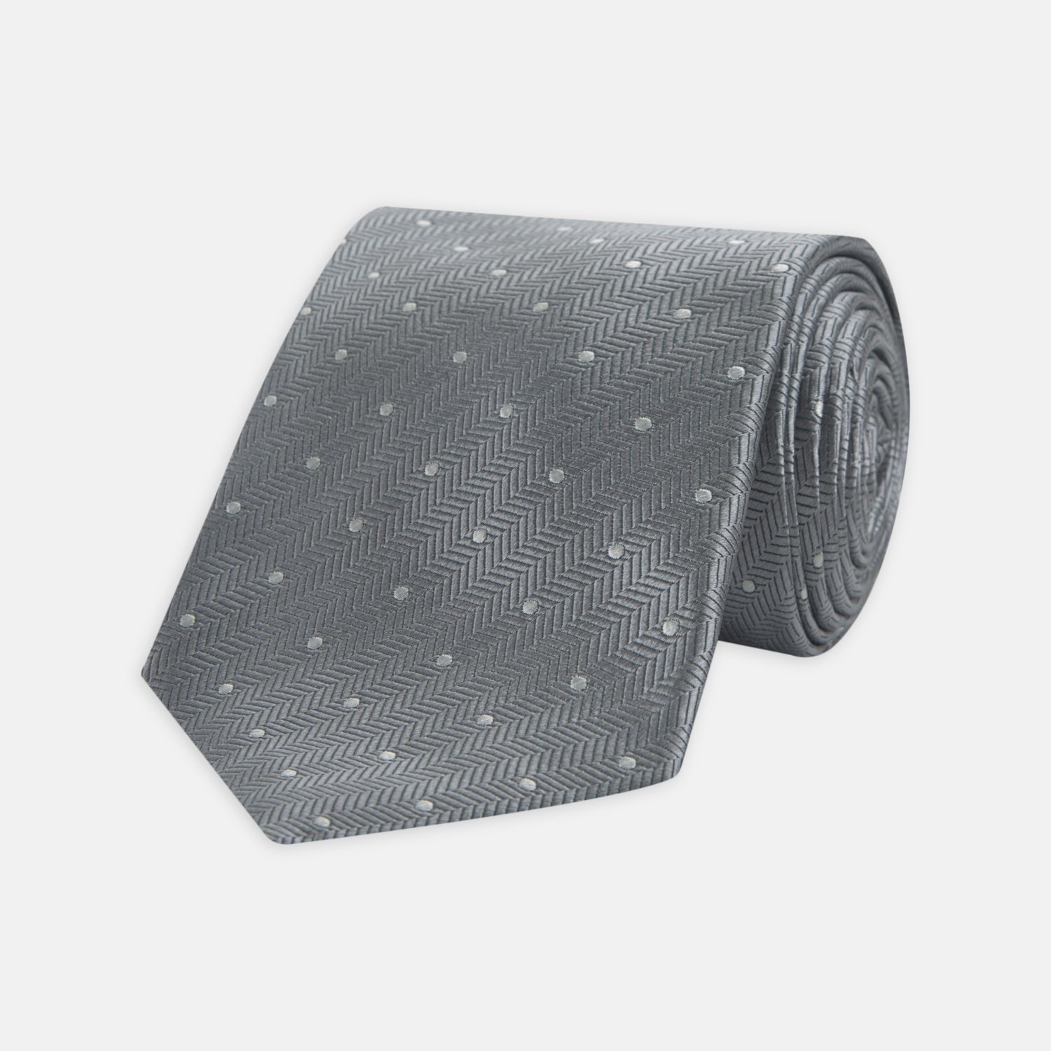 View 1 of product The Turnbull & Asser Grey and White Small Spot Herringbone Silk Tie, expertly woven from silk, is displayed rolled-up against a white background.