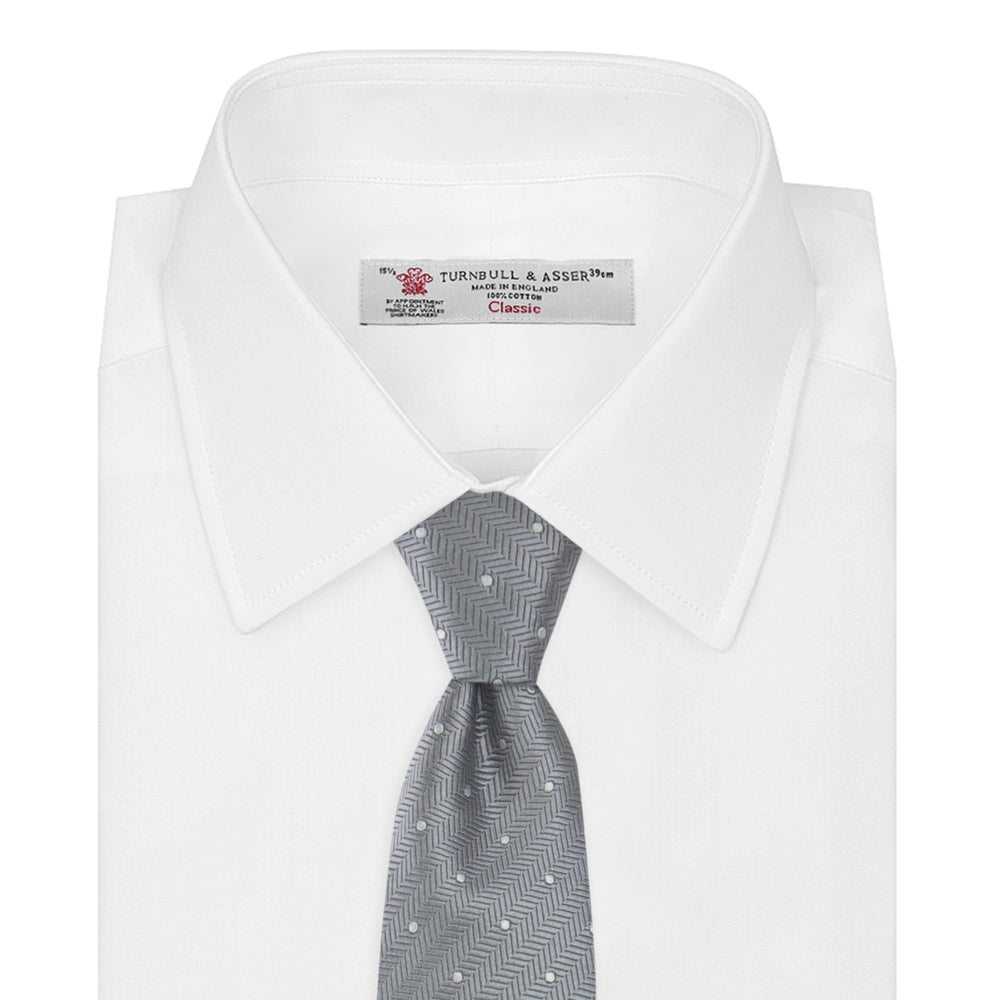 The Turnbull & Asser Grey and White Small Spot Herringbone Silk Tie, expertly woven from silk, is displayed rolled-up against a white background.