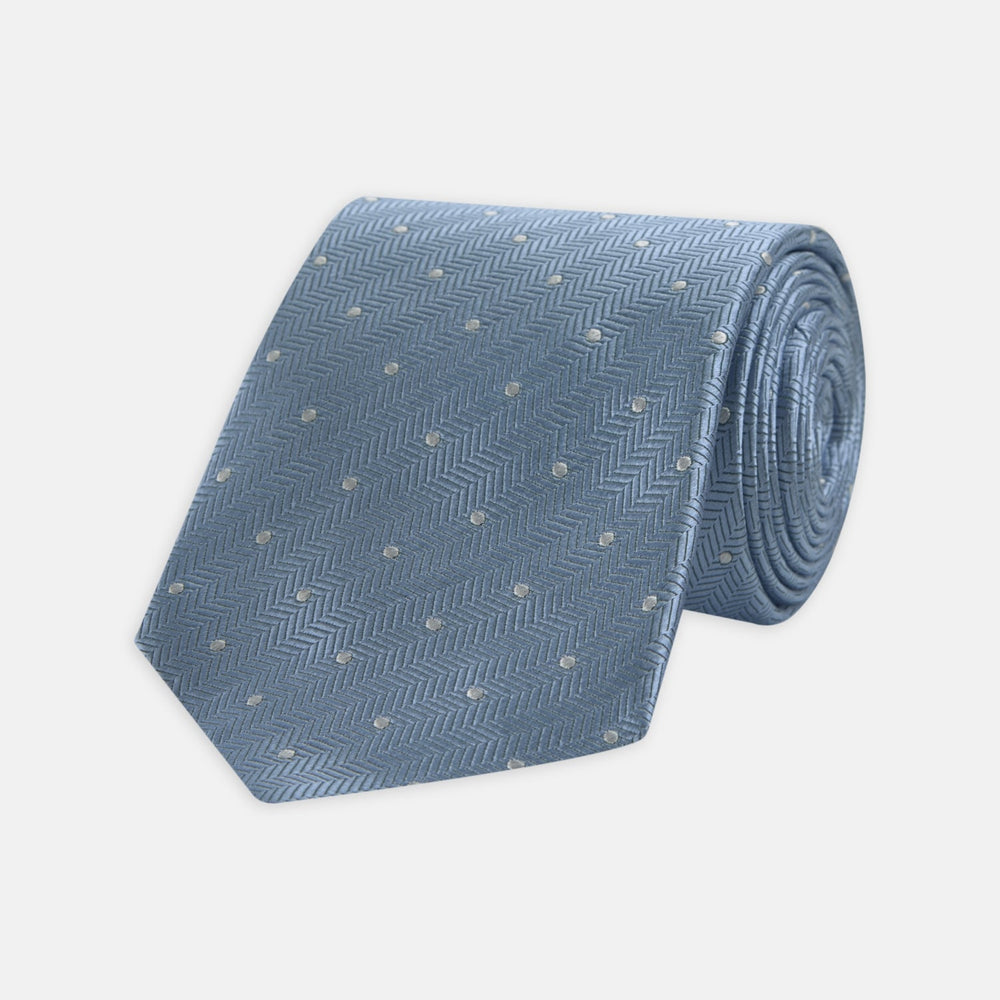The Turnbull & Asser Ice Blue and White Small Spot Herringbone Silk Tie features a refined herringbone weave with subtle white spots, displayed elegantly against a plain white background.