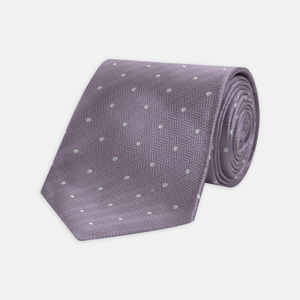 The Turnbull & Asser Lilac and White Small Spot Herringbone Silk Tie, crafted from fine English silk, is neatly rolled and displayed on a plain white background.