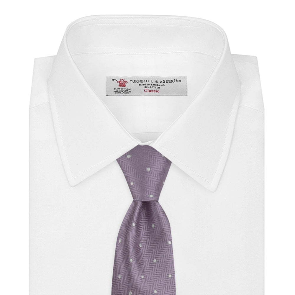 The Turnbull & Asser Lilac and White Small Spot Herringbone Silk Tie, crafted from fine English silk, is neatly rolled and displayed on a plain white background.