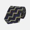 View 1 of product The Navy and Gold Striped Zigzag Silk Tie by Turnbull & Asser features a bold geometric pattern—an essential modern accessory shown rolled up with the pointed end forward on a white background.