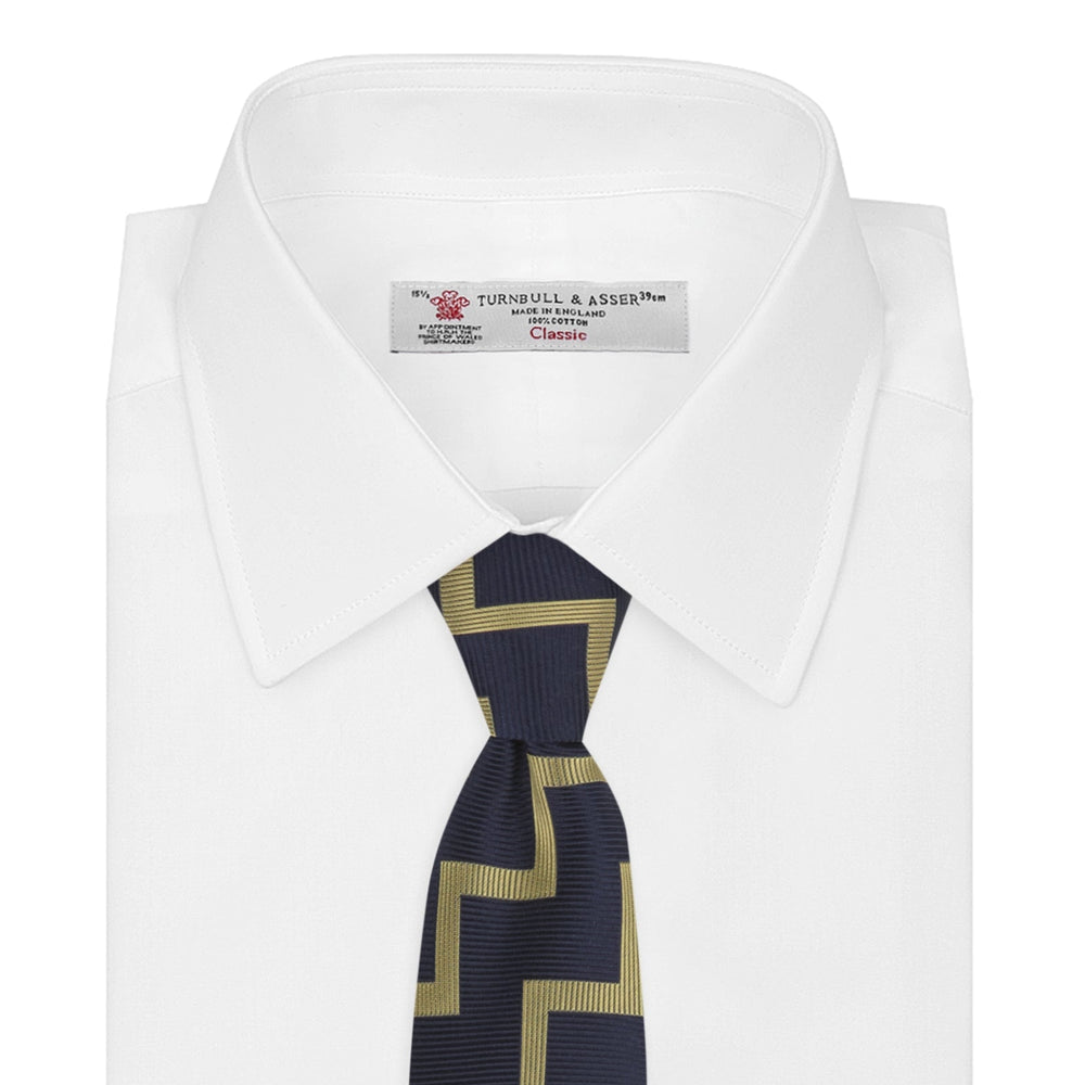 The Navy and Gold Striped Zigzag Silk Tie by Turnbull & Asser features a bold geometric pattern—an essential modern accessory shown rolled up with the pointed end forward on a white background.