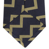View 4 of product The Navy and Gold Striped Zigzag Silk Tie by Turnbull & Asser features a bold geometric pattern—an essential modern accessory shown rolled up with the pointed end forward on a white background.