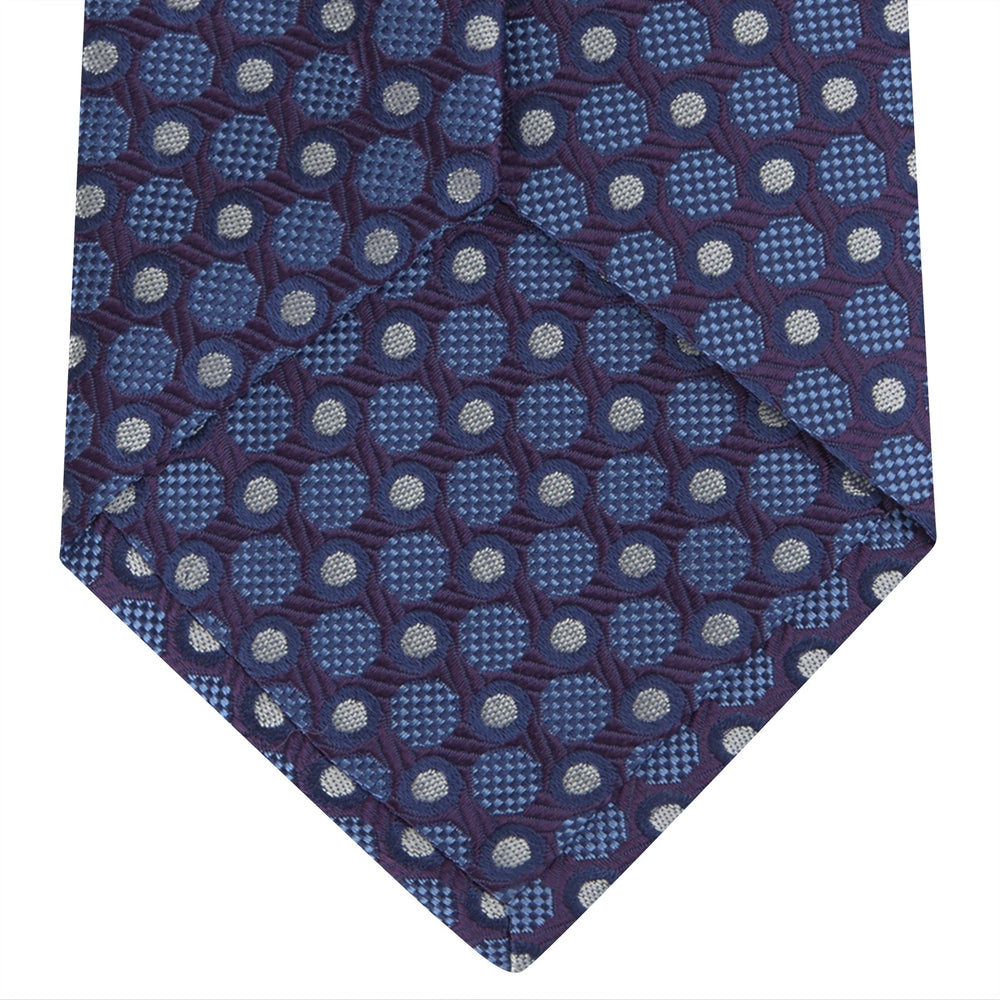 The Turnbull & Asser Plum and Blue Circle and Spot Silk Tie, shown rolled up on a white background, features a classic pattern—an elegant choice to complement any office shirt.