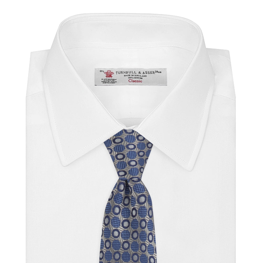 The Turnbull & Asser Silver and Blue Circle and Spot Silk Tie features a classic geometric pattern in silver and light blue on white, making it the perfect complement to any office shirt.