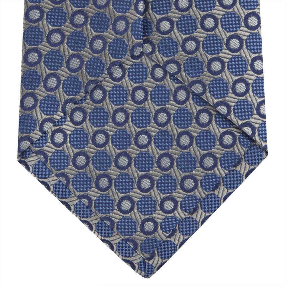 The Turnbull & Asser Silver and Blue Circle and Spot Silk Tie features a classic geometric pattern in silver and light blue on white, making it the perfect complement to any office shirt.