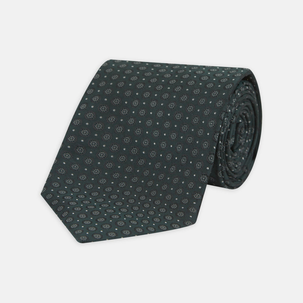 The Turnbull & Asser Forest Green Floral Spot Silk Tie features a subtle light gray circular pattern, shown rolled on a white background—a classic accessory ideal for office shirts.
