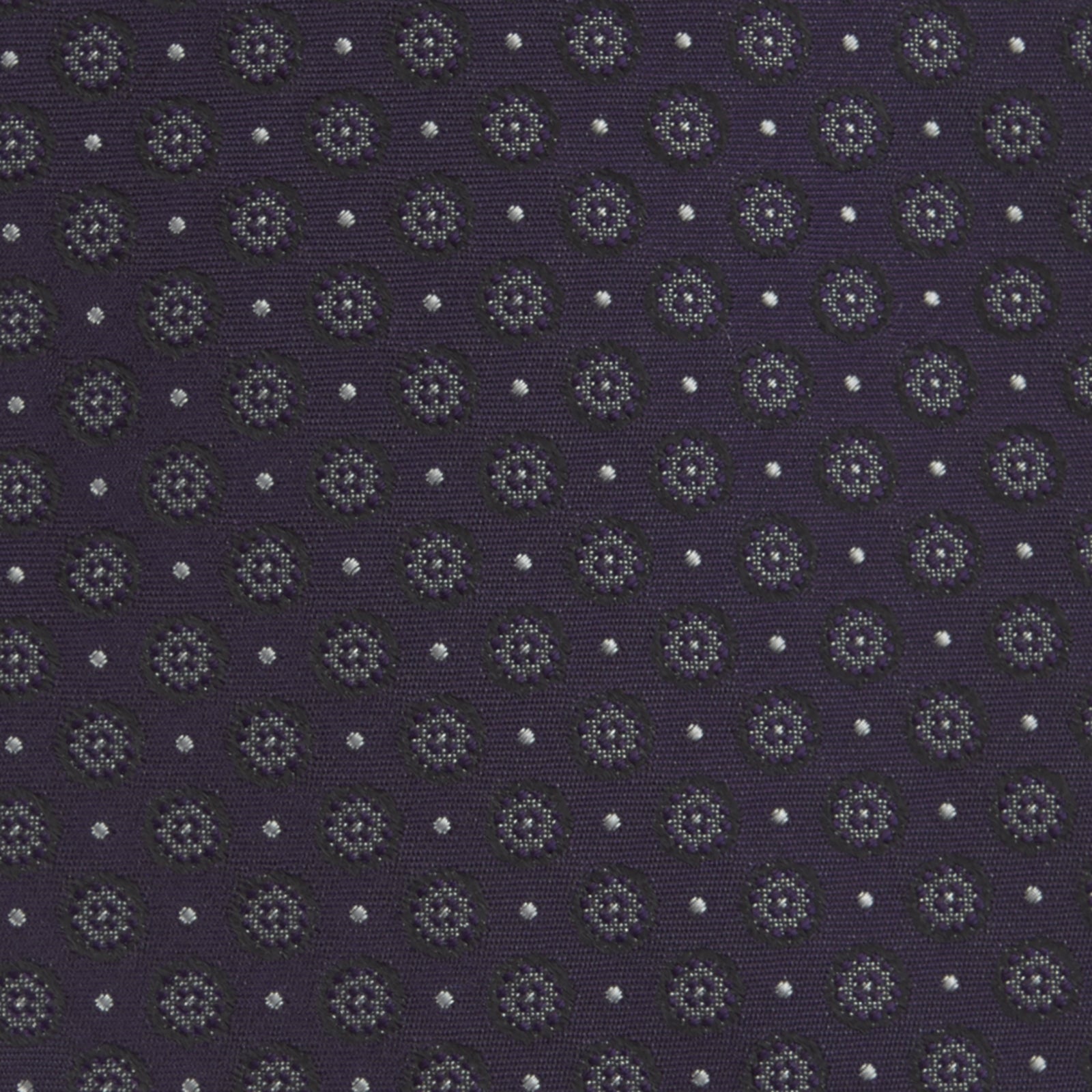 View 3 of product The Turnbull & Asser Plum Floral Spot Silk Tie features a rolled-up classic design with small, evenly spaced floral spots in lighter purple and white, ideal for office shirts and shown against a plain white background.