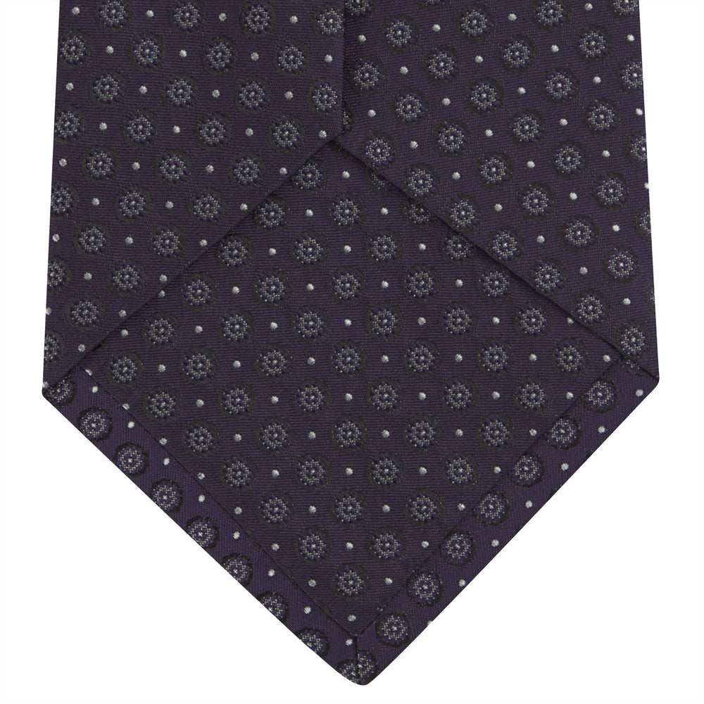 The Turnbull & Asser Plum Floral Spot Silk Tie features a rolled-up classic design with small, evenly spaced floral spots in lighter purple and white, ideal for office shirts and shown against a plain white background.
