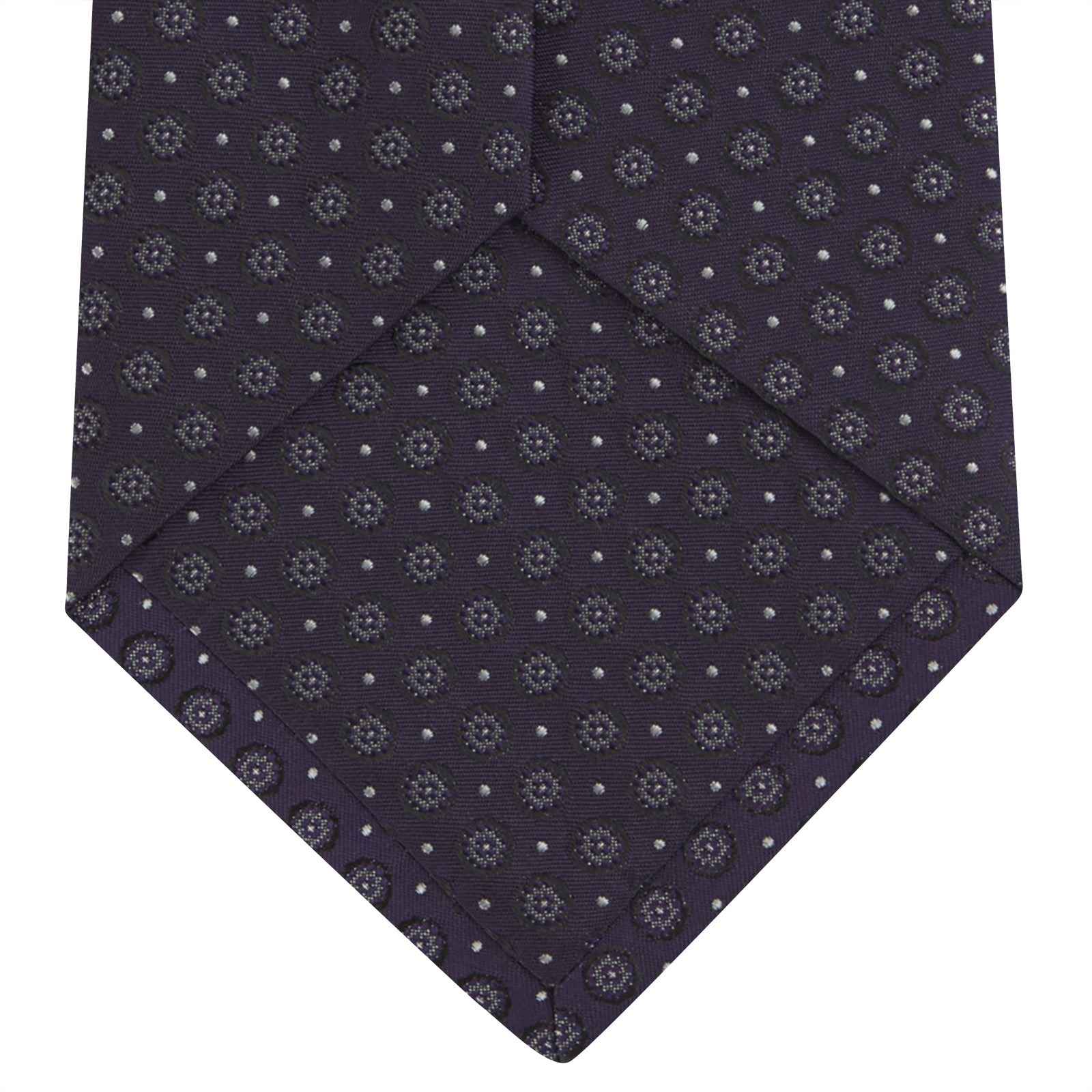 View 4 of product The Turnbull & Asser Plum Floral Spot Silk Tie features a rolled-up classic design with small, evenly spaced floral spots in lighter purple and white, ideal for office shirts and shown against a plain white background.