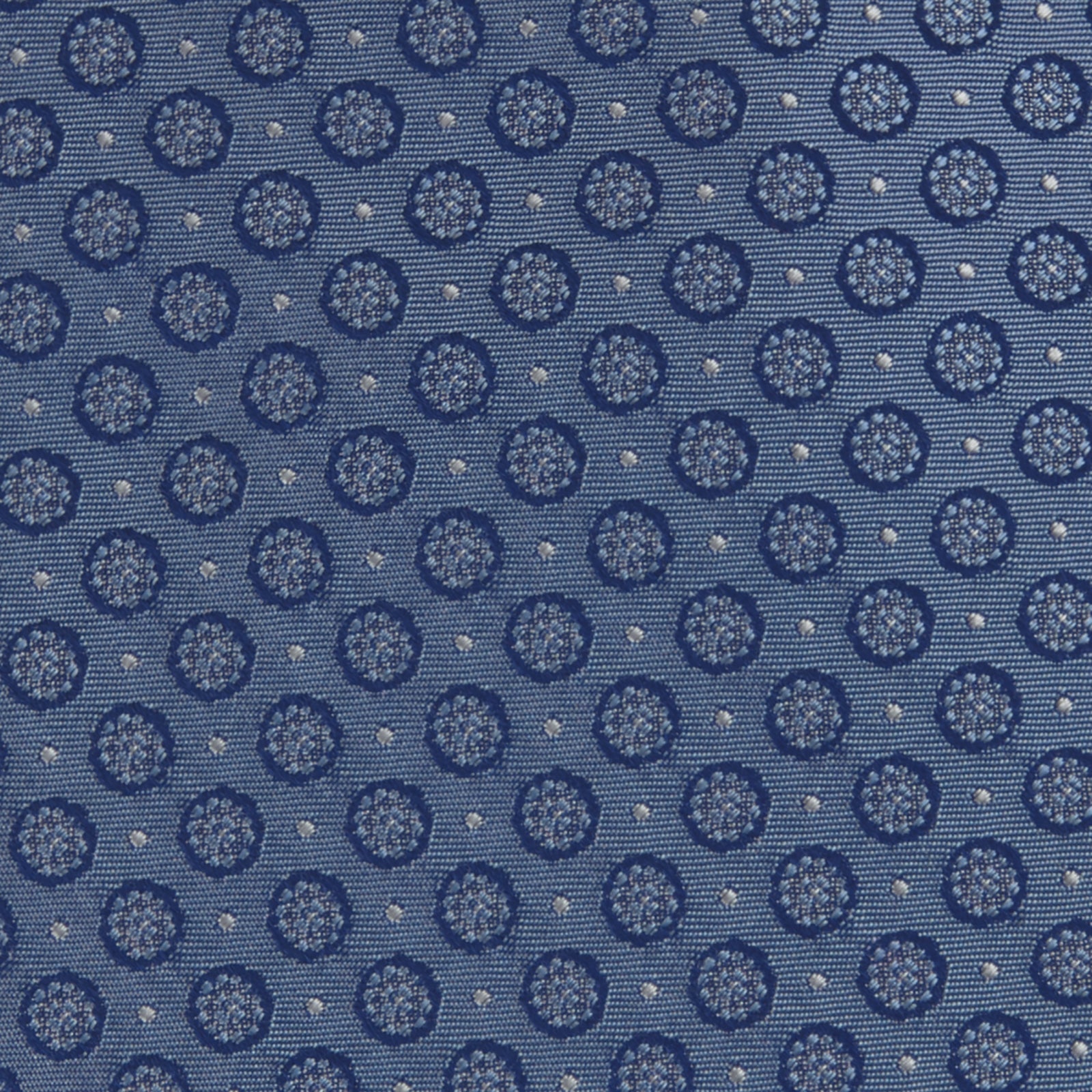 View 3 of product The Light Blue Floral Spot Silk Tie by Turnbull & Asser features a classic pattern in varied blue tones, rolled up on a white background—an ideal accessory to complement any office shirt.
