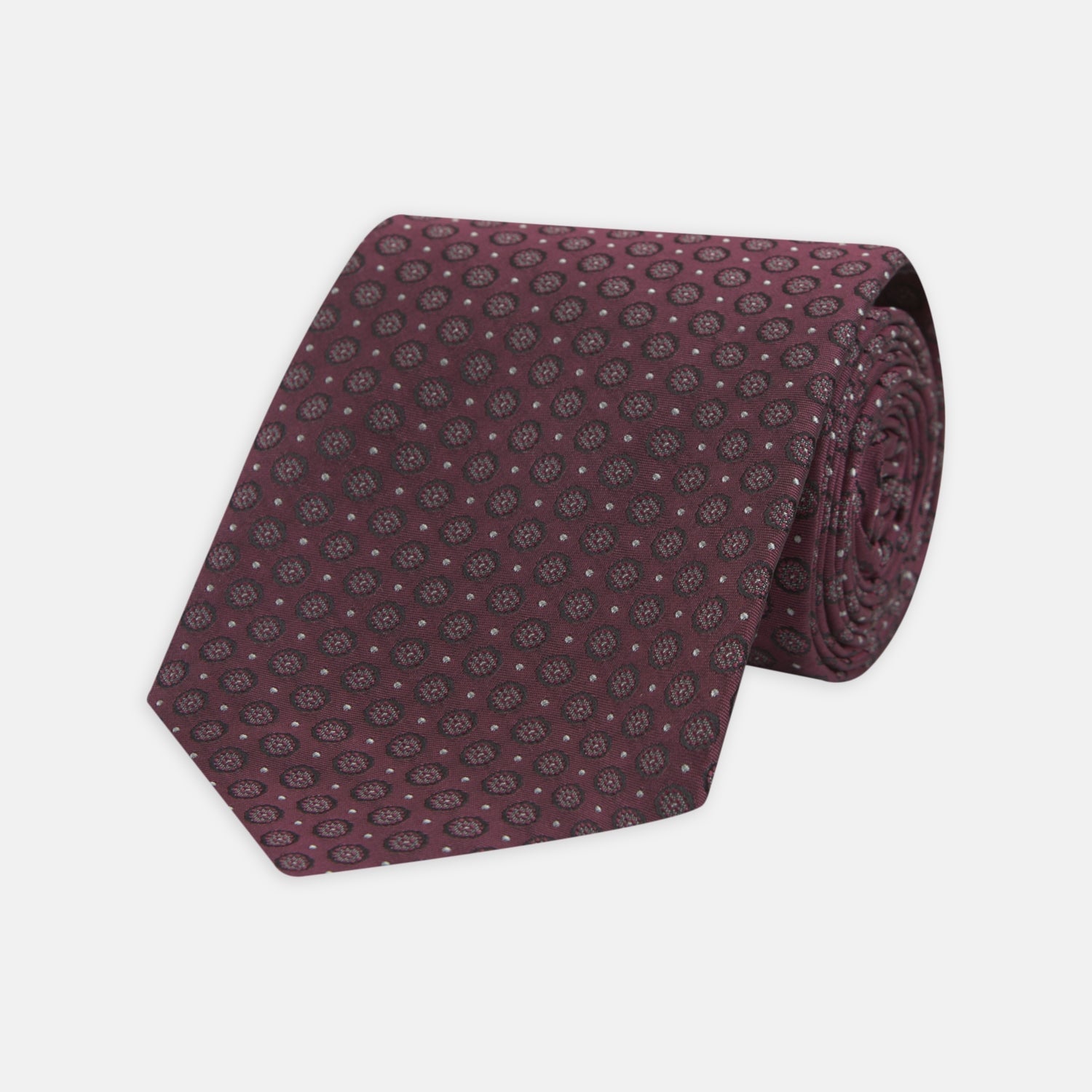 View 1 of product The Turnbull & Asser Wine Floral Spot Silk Tie features a rolled design with a gray and black circular pattern, perfect for the office. Displayed on a plain white background.