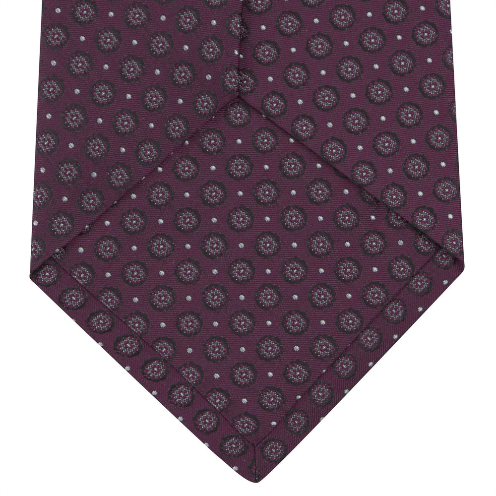 The Turnbull & Asser Wine Floral Spot Silk Tie features a rolled design with a gray and black circular pattern, perfect for the office. Displayed on a plain white background.