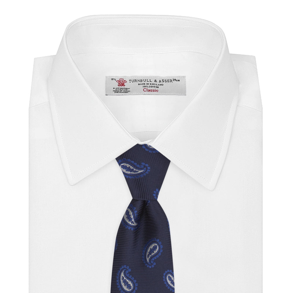 The Turnbull & Asser Navy and Royal Blue Floating Paisley Silk Tie features an elegant blue and white paisley pattern, styled in a rolled presentation on a plain white background.