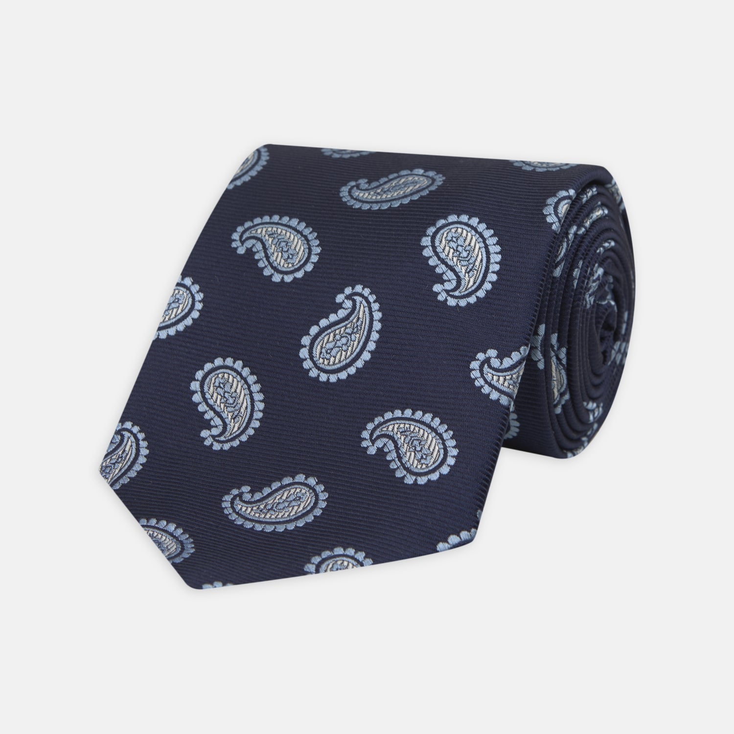 View 1 of product The Turnbull & Asser Navy and Light Blue Floating Paisley Silk Tie features a repeating light blue and white paisley pattern set against a navy blue silk backdrop.