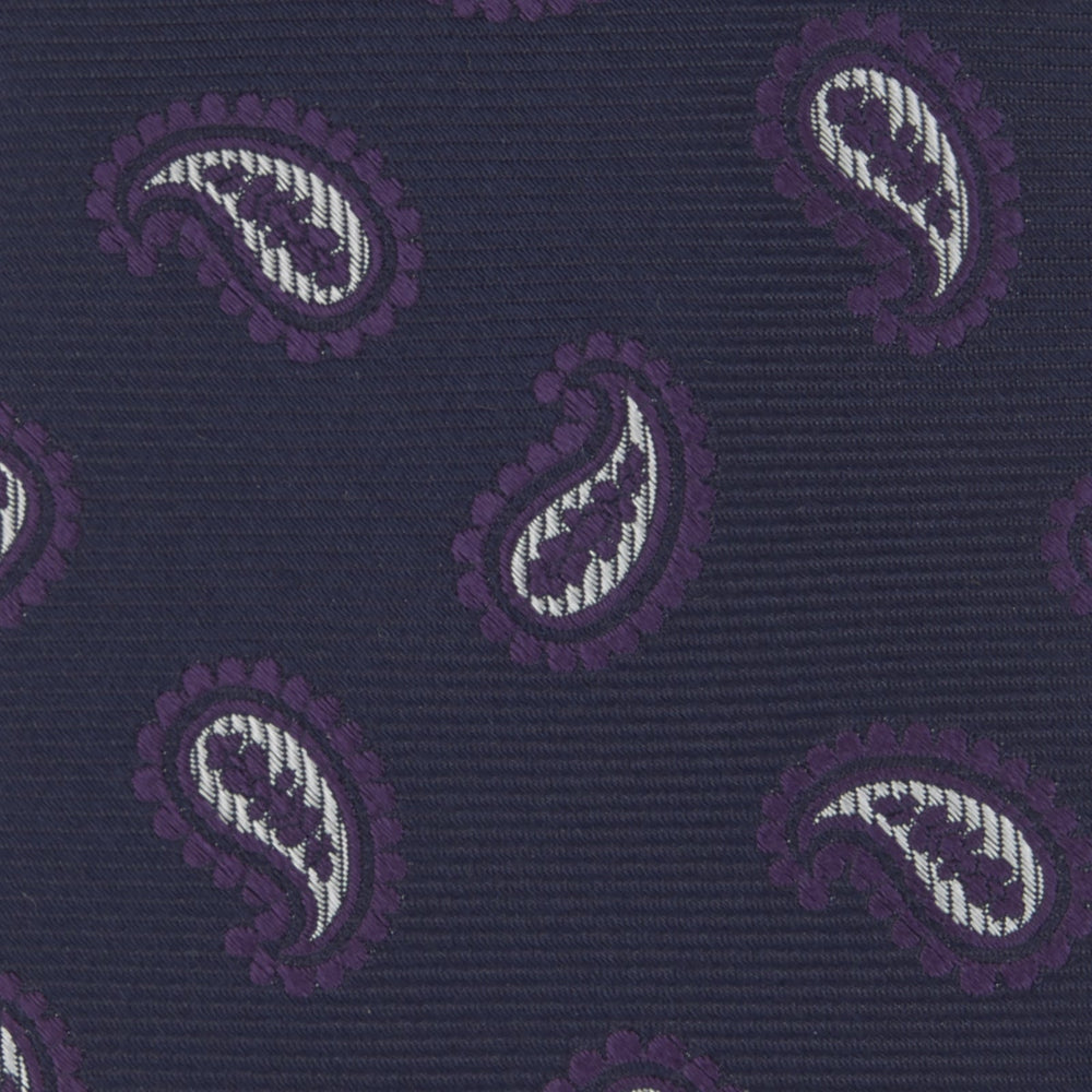 The Turnbull & Asser Navy and Plum Floating Paisley Silk Tie features a repeating purple and white paisley pattern, elegantly rolled up on a white background.