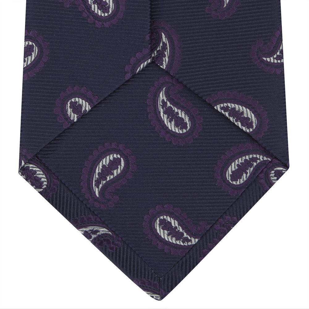 The Turnbull & Asser Navy and Plum Floating Paisley Silk Tie features a repeating purple and white paisley pattern, elegantly rolled up on a white background.