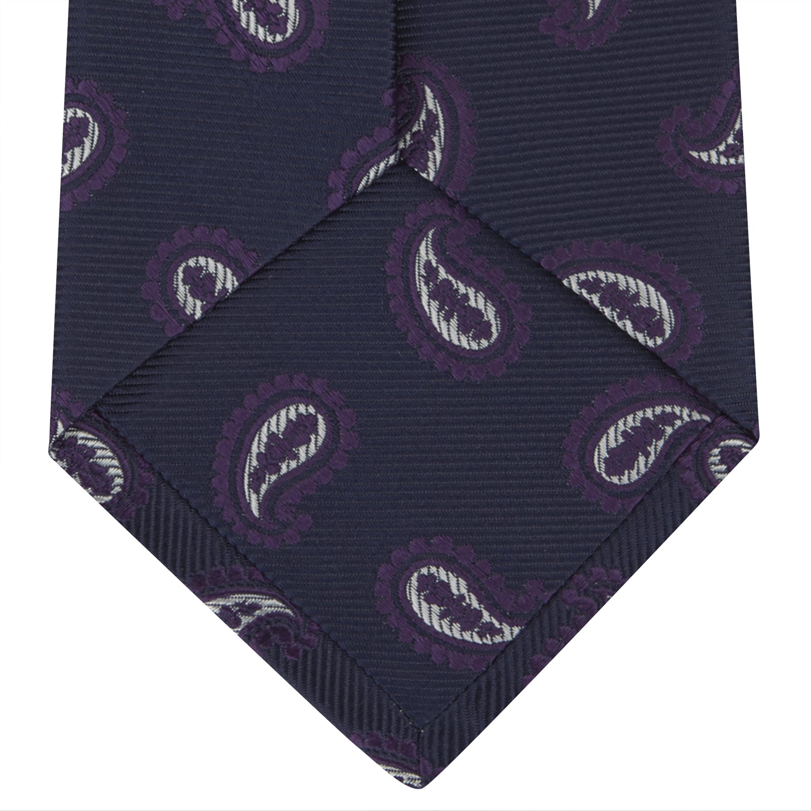 View 4 of product The Turnbull & Asser Navy and Plum Floating Paisley Silk Tie features a repeating purple and white paisley pattern, elegantly rolled up on a white background.