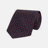 View 1 of product The Turnbull & Asser Navy and Red Paint Spot Silk Tie, featuring red spots on navy blue silk, is rolled with the wide end forward—ideal for office shirts and shown against a white background.