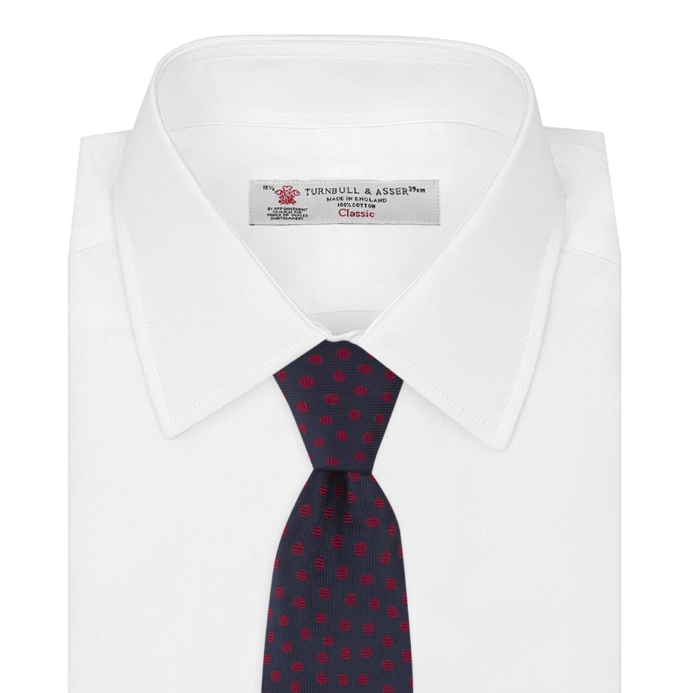 The Turnbull & Asser Navy and Red Paint Spot Silk Tie, featuring red spots on navy blue silk, is rolled with the wide end forward—ideal for office shirts and shown against a white background.