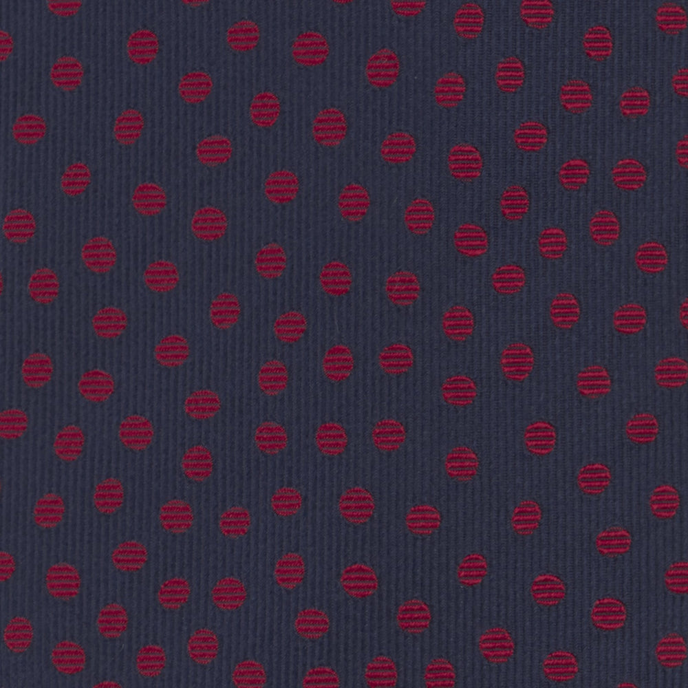 The Turnbull & Asser Navy and Red Paint Spot Silk Tie, featuring red spots on navy blue silk, is rolled with the wide end forward—ideal for office shirts and shown against a white background.
