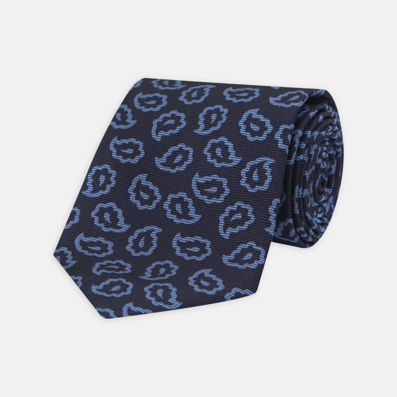 View 1 of product The Navy and Blue Petal Paisley Silk Tie by Turnbull & Asser features an abstract pattern of light blue paisley-like shapes, rolled up and displayed on a white background.