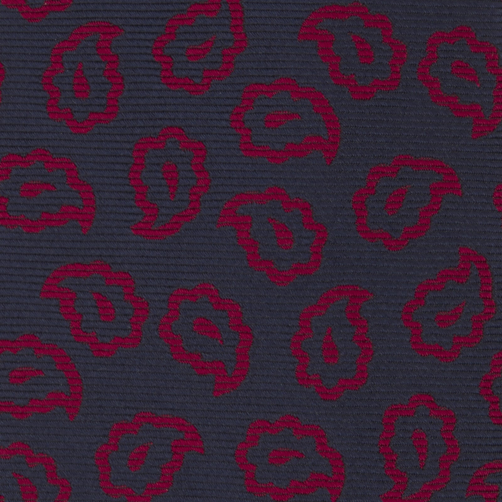 View 3 of product The Navy and Red Petal Paisley Silk Tie by Turnbull & Asser features an elegant paisley pattern on navy silk, rolled at one end and displayed on a plain white background.