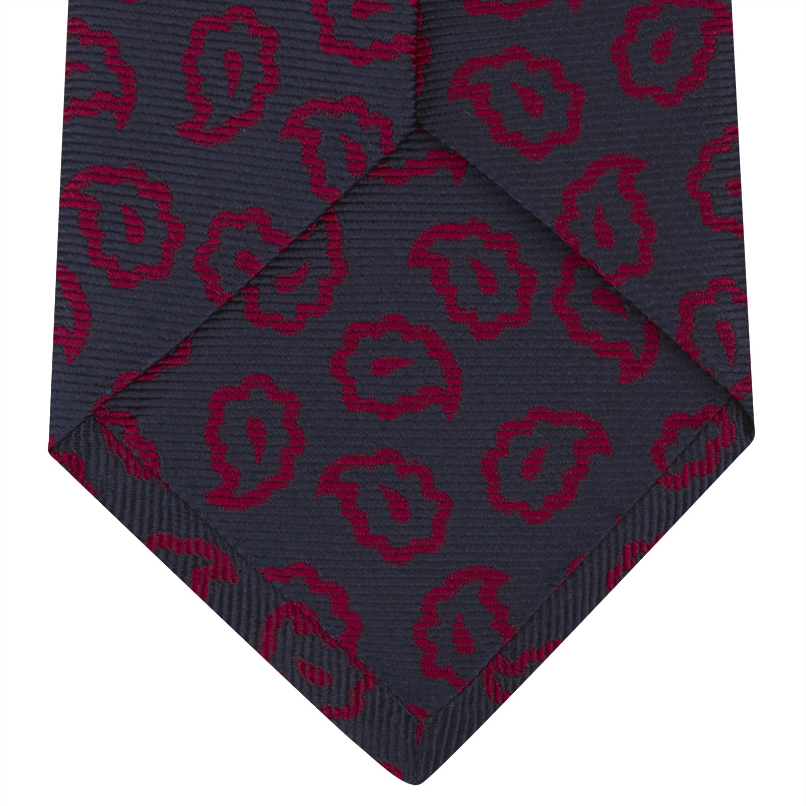 View 4 of product The Navy and Red Petal Paisley Silk Tie by Turnbull & Asser features an elegant paisley pattern on navy silk, rolled at one end and displayed on a plain white background.