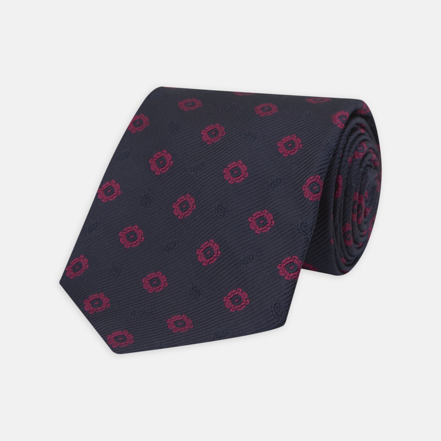 View 1 of product The Turnbull & Asser Navy and Dark Pink Emblem Spot Silk Tie features a classic pattern of small, evenly spaced emblems—ideal for complementing your favorite office shirt.