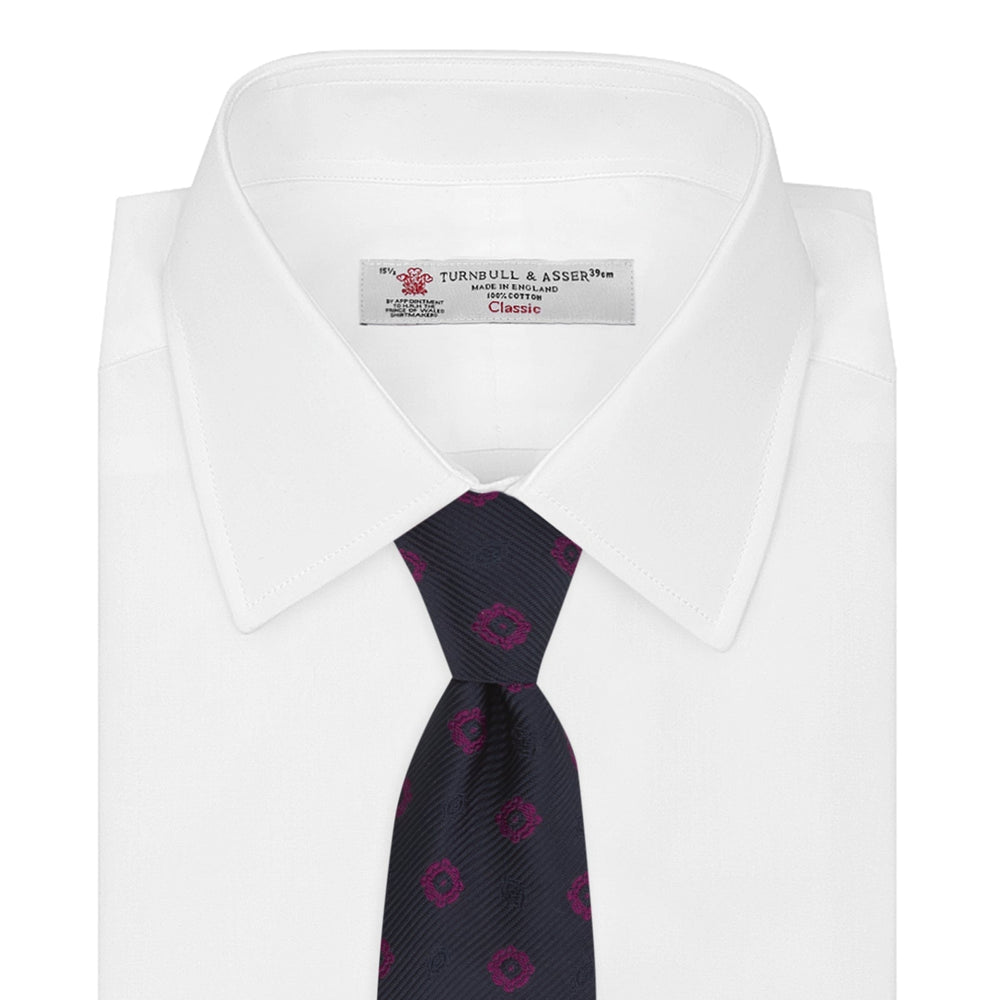 The Turnbull & Asser Navy and Dark Pink Emblem Spot Silk Tie features a classic pattern of small, evenly spaced emblems—ideal for complementing your favorite office shirt.