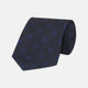 The Turnbull & Asser Navy and Blue Emblem Spot Silk Tie features a classic pattern of light blue motifs on navy silk, showcased rolled on a white background—a refined accessory for any office shirt.