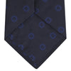 View 4 of product The Turnbull & Asser Navy and Blue Emblem Spot Silk Tie features a classic pattern of light blue motifs on navy silk, showcased rolled on a white background—a refined accessory for any office shirt.