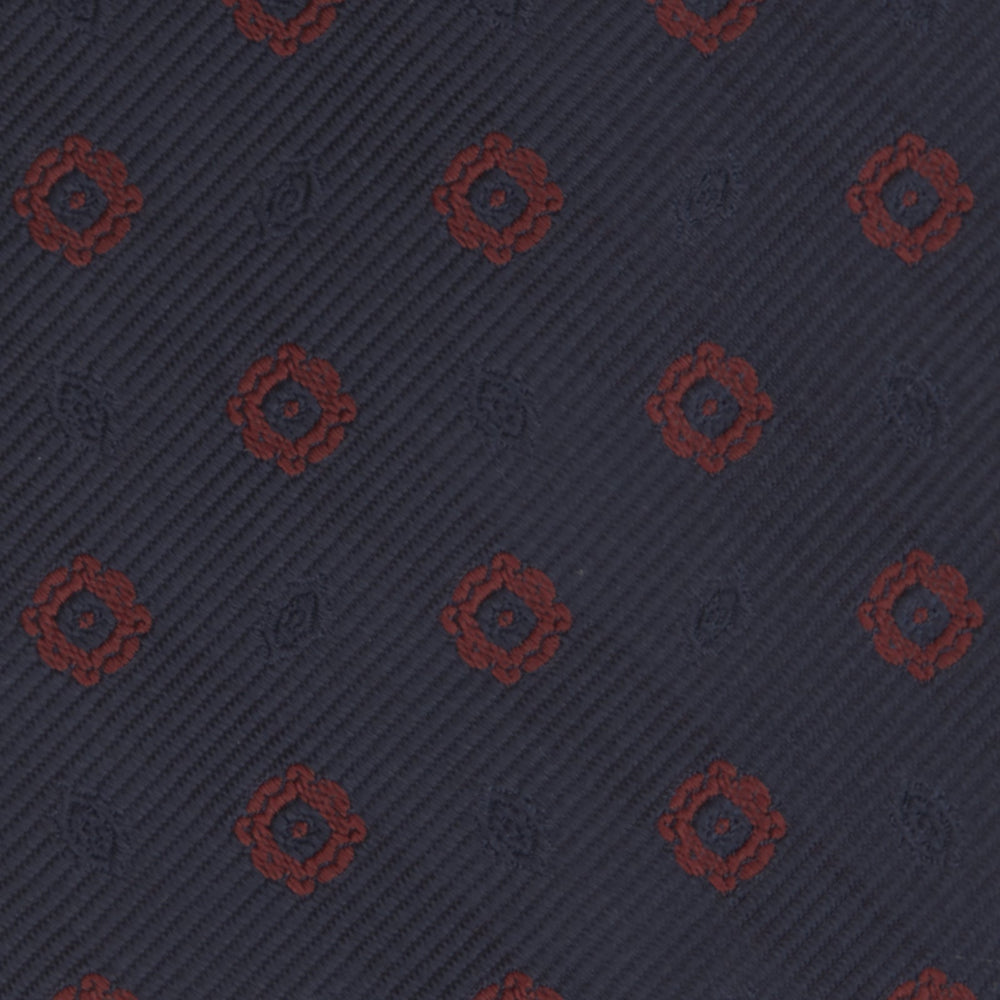 The Turnbull & Asser Navy and Burgundy Emblem Spot Silk Tie features a subtle textured pattern with small burgundy emblems on navy silk. Perfectly rolled with a pointed tip, it pairs well with any office shirt.