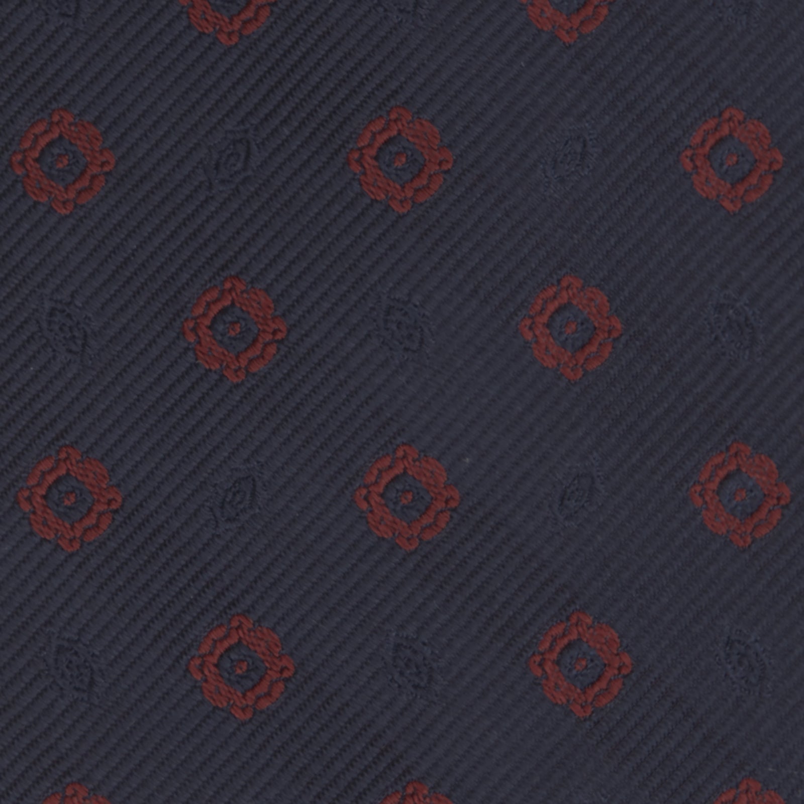 View 3 of product The Turnbull & Asser Navy and Burgundy Emblem Spot Silk Tie features a subtle textured pattern with small burgundy emblems on navy silk. Perfectly rolled with a pointed tip, it pairs well with any office shirt.