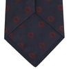View 4 of product The Turnbull & Asser Navy and Burgundy Emblem Spot Silk Tie features a subtle textured pattern with small burgundy emblems on navy silk. Perfectly rolled with a pointed tip, it pairs well with any office shirt.