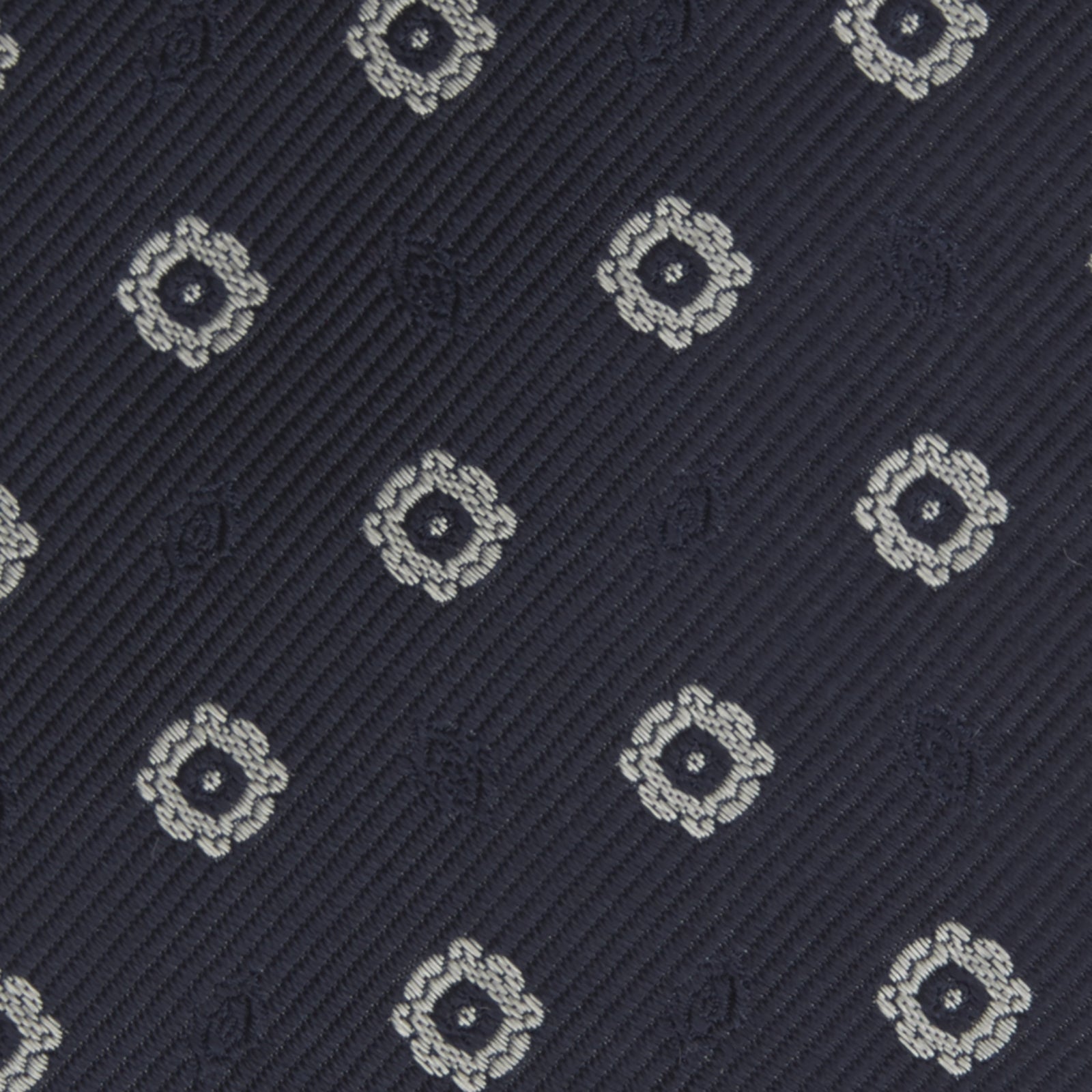 View 3 of product The Turnbull & Asser Navy and Silver Emblem Spot Silk Tie features a refined repeating emblem pattern in silver on navy silk, making it an elegant accessory for any office shirt.