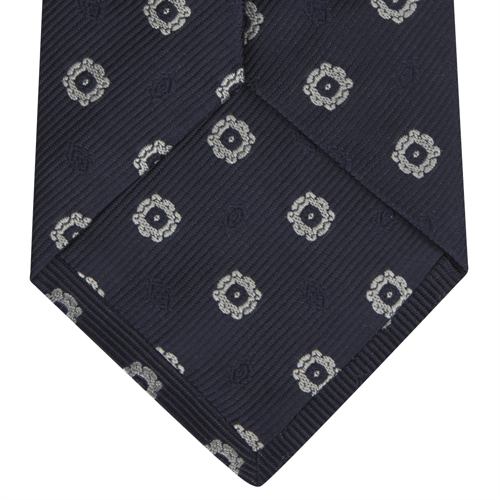 View 4 of product The Turnbull & Asser Navy and Silver Emblem Spot Silk Tie features a refined repeating emblem pattern in silver on navy silk, making it an elegant accessory for any office shirt.