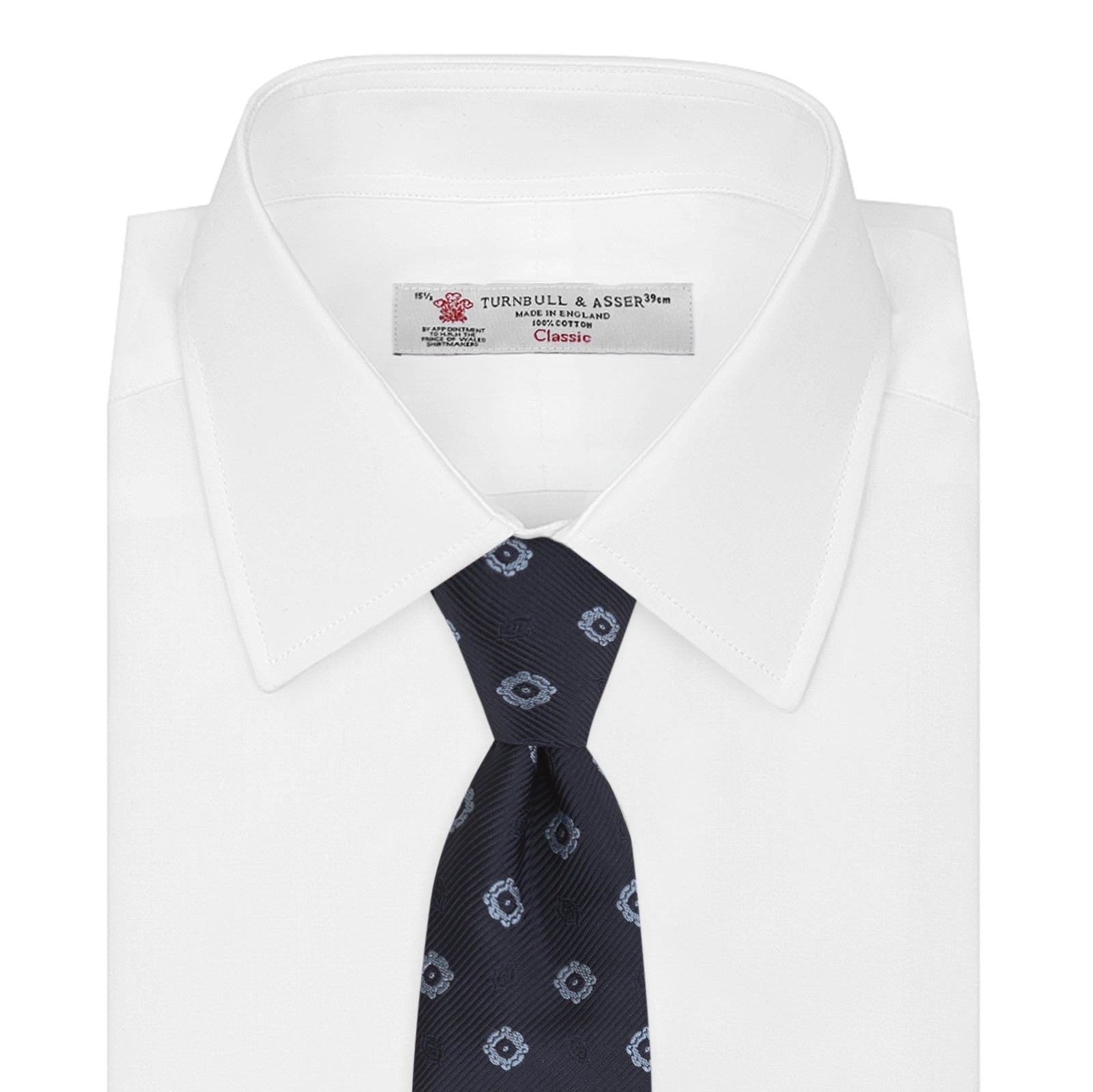 View 2 of product The Turnbull & Asser Navy and Light Blue Emblem Spot Silk Tie features a classic rolled design with a repeating light blue emblem pattern, ideal for office wear, shown against a plain white background.