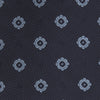 View 3 of product The Turnbull & Asser Navy and Light Blue Emblem Spot Silk Tie features a classic rolled design with a repeating light blue emblem pattern, ideal for office wear, shown against a plain white background.