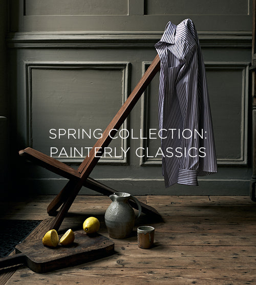 A striped button-up shirt draped over a wooden chair, with lemons, a ceramic jug, and a cup on a rustic wooden floor. Text reads: “Spring Collection: Painterly Classics.”.