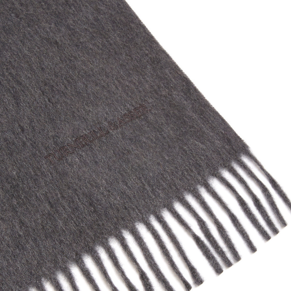 A sartorial essential, the Turnbull & Asser Dark Grey Pure Cashmere Scarf features fringed ends and is shown neatly folded on a plain white background.