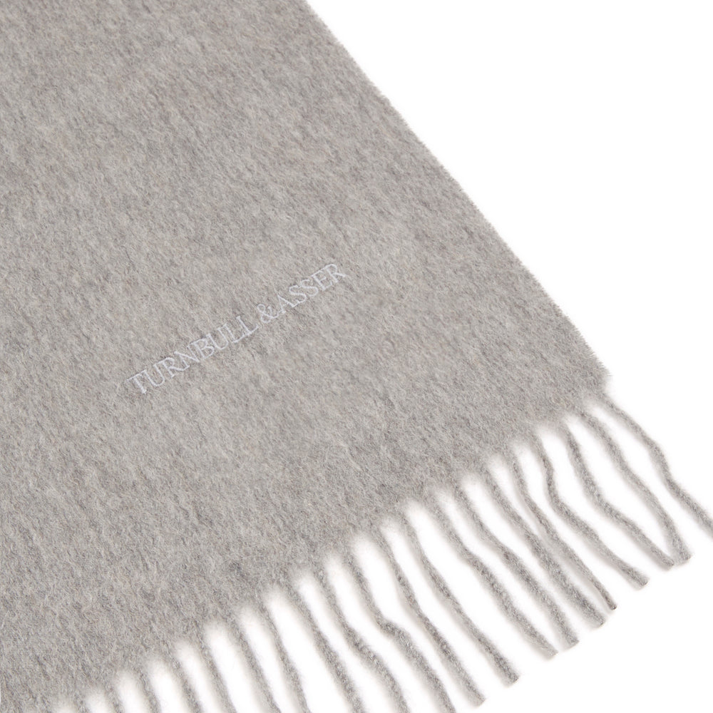 The Flannel Grey Pure Cashmere Scarf by Turnbull & Asser is crafted from soft cashmere, showcased neatly folded with fringed ends on a plain white background.